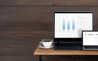 Laptop mit Analytics-Dashboard, Notizblock mit handschriftlichen Notizen und Kaffeetasse auf Holztisch.